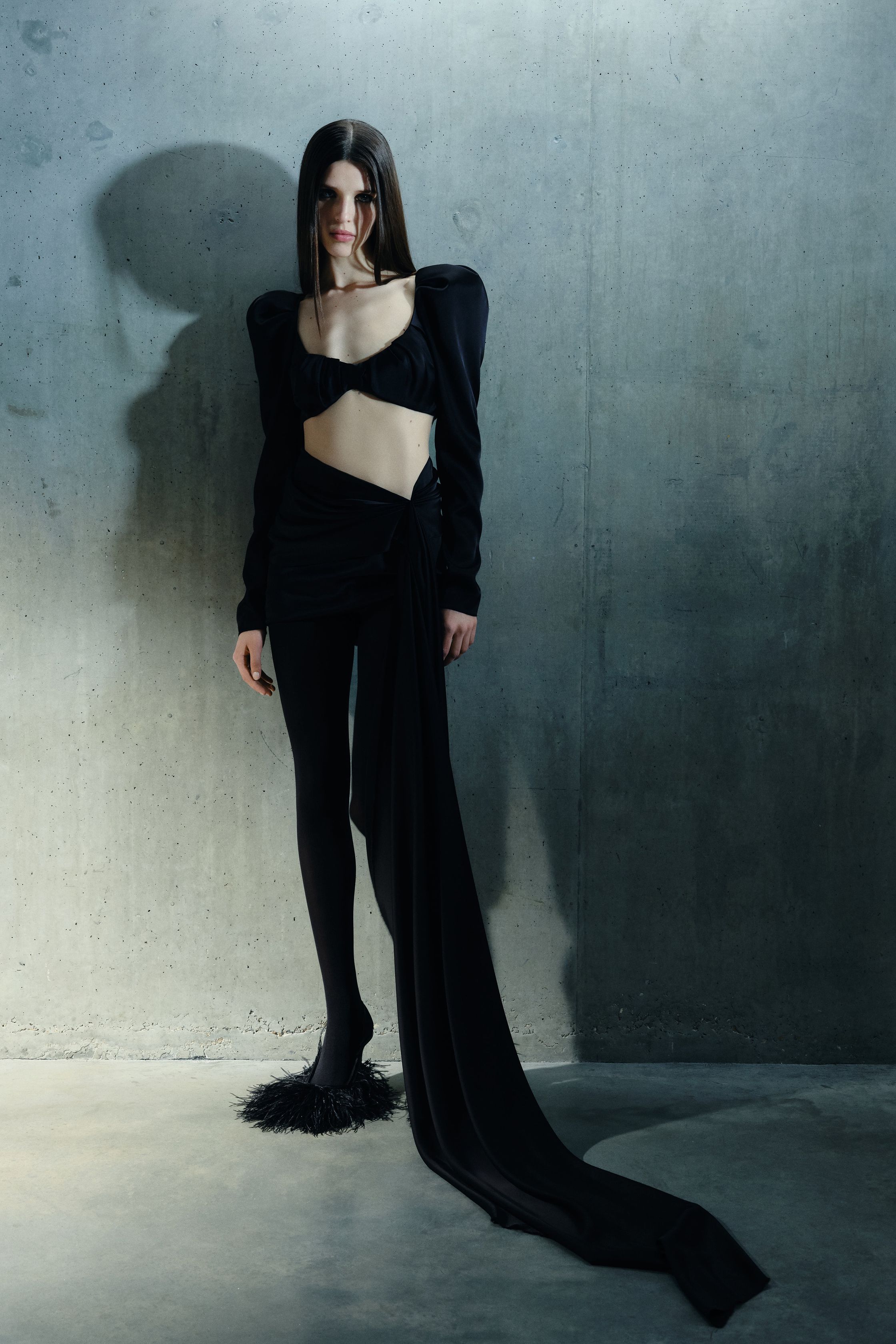 David Koma 2026秋冬以极具力量感的黑白礼服系列展现品牌标志性性感：羽毛、结构肩线与紧身剪裁共同塑造强烈女性形象。黑色连体礼服、雕塑式裙装与链条装饰构建出带有夜晚气质的时装世界。整体轮廓强调修长比例与戏剧化细节，使女性身体成为服装设计的中心-顽石频道趋势研究